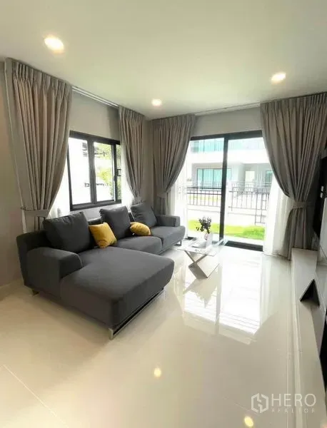 Detached House for rent - Bright living room with gray sectional sofa and sliding glass doors opening to a small garden.