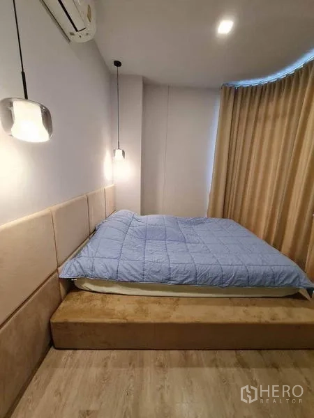 คอนโด ให้เช่า - ภาพระยะใกล้ของหัวเตียงบุผ้า โคมไฟห้อย และเตียงโทนสีอบอุ่น