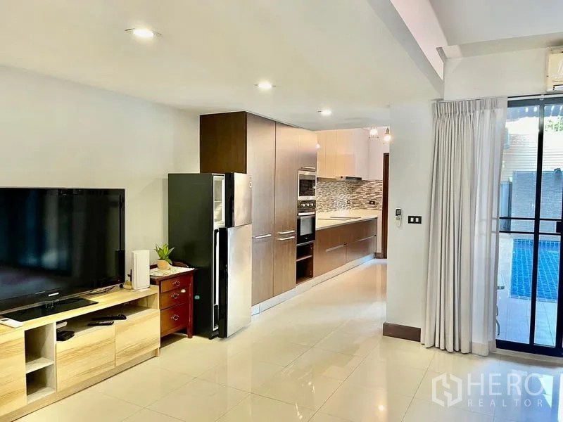 Townhouse for rent in Khlong Toei, Bangkok - Open-plan living with built-in kitchen, modern appliances, and access to the pool through glass doors.