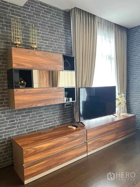 คอนโด ให้เช่าหรือขายในWatthana, Bangkok - มุมนั่งเล่น ผนังอิฐตกแต่ง ตู้ทีวีลายไม้ และทีวีจอแบนข้างผ้าม่านสูง