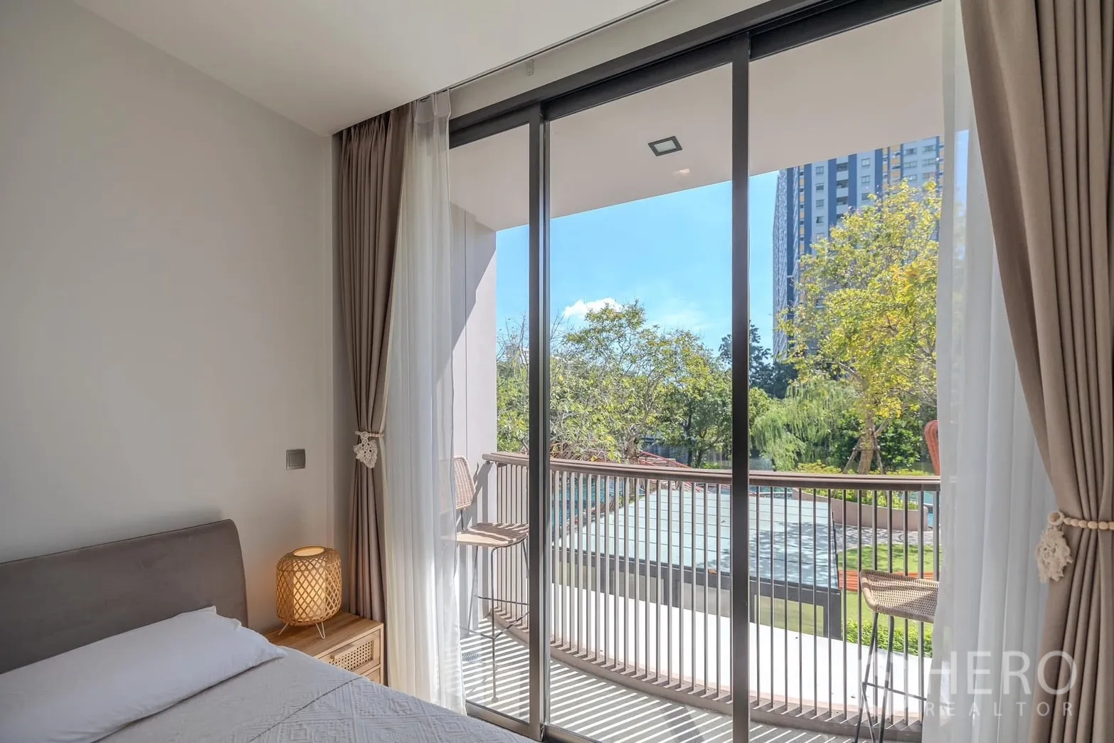 Condominium for rent in Watthana, Bangkok - Bedroom opening to a balcony with chairs and views of trees and the pool area.