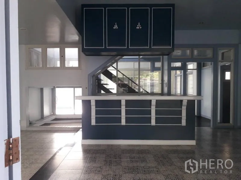 บ้าน ให้เช่าในWatthana, Bangkok - พื้นที่นั่งเล่นแบบเปิดโล่งพร้อมเคาน์เตอร์บิวท์อินและบันไดใต้ตู้สีเข้ม