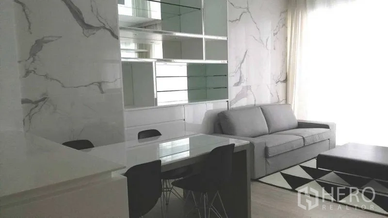 Condominium for rent in Pathum Wan, Bangkok - Dining nook with glass-front cabinets and marble wall beside a two-seat sofa.