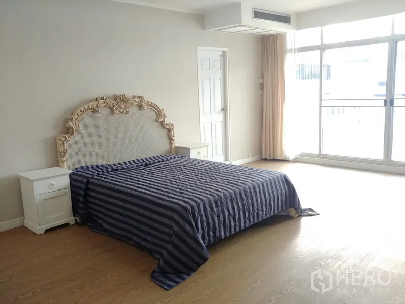 公寓 出租或出售在Watthana, Bangkok - 卧室配雕花床头与床头柜，落地推拉门通向阳台。