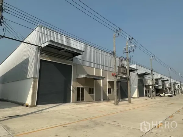 Factory for rent in Bang Phli, Samut Prakan - Modern factory row with large roller shutters, metal cladding and a wide concrete driveway.