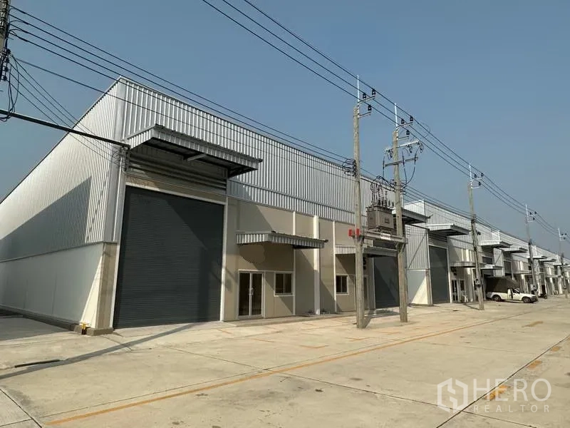 Factory for rent in Bang Phli, Samut Prakan - Modern factory row with large roller shutters, metal cladding and a wide concrete driveway.