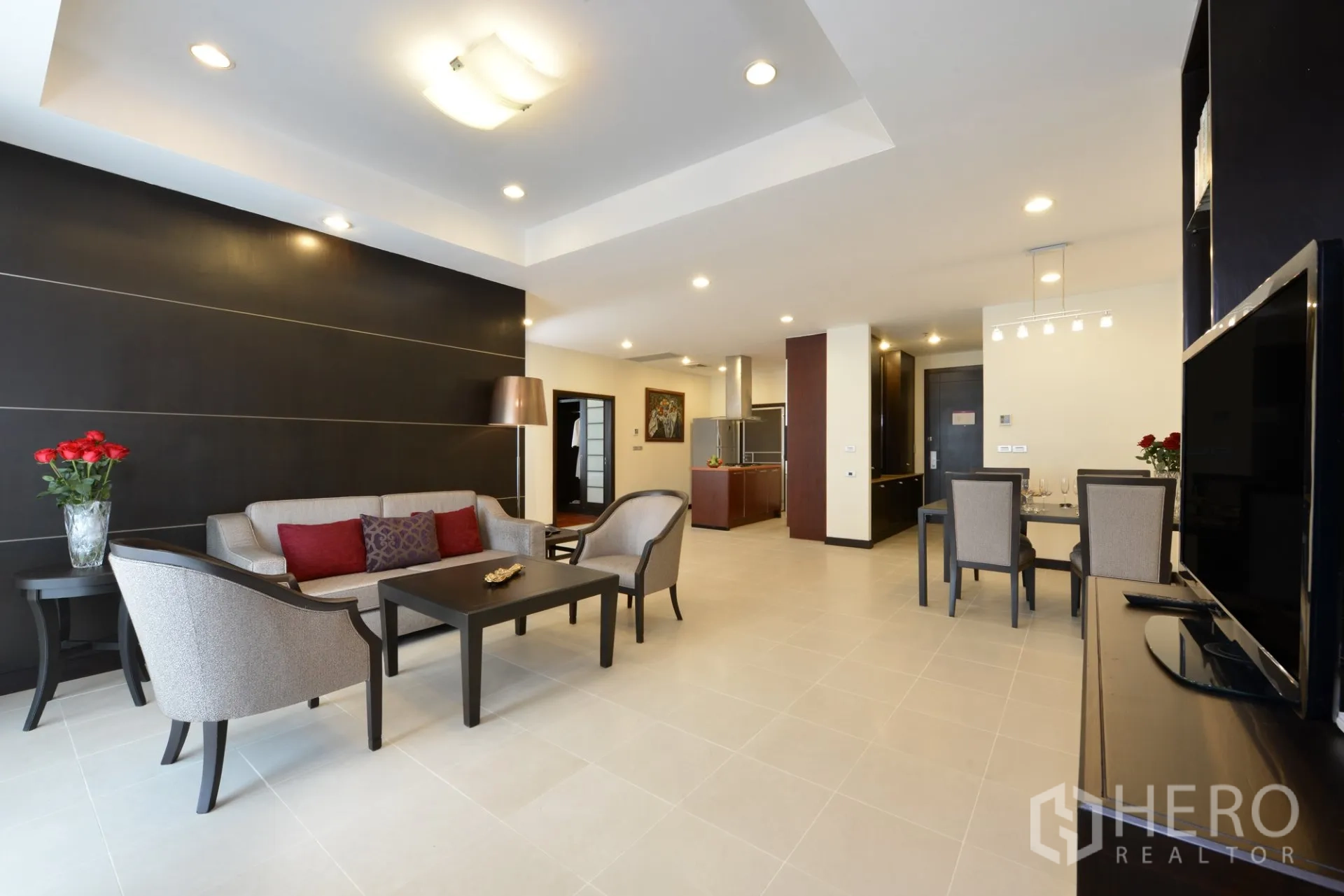 Apartment for rent in Watthana, Bangkok - Open-plan living and dining area with sofa set, feature wall, TV console, and recessed lighting.