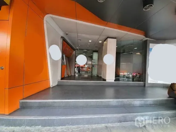 店屋 出租在Bang Rak, Bangkok - 现代商铺入口，橙色立面、台阶与玻璃门面。