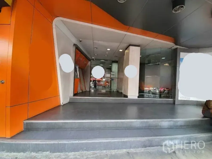 店屋 出租在Bang Rak, Bangkok - 现代商铺入口，橙色立面、台阶与玻璃门面。