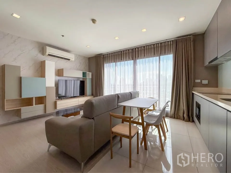 Condominium for rent in Khlong Toei, Bangkok - Open-plan living area with L-shaped sofa, dining table, TV wall and kitchenette.