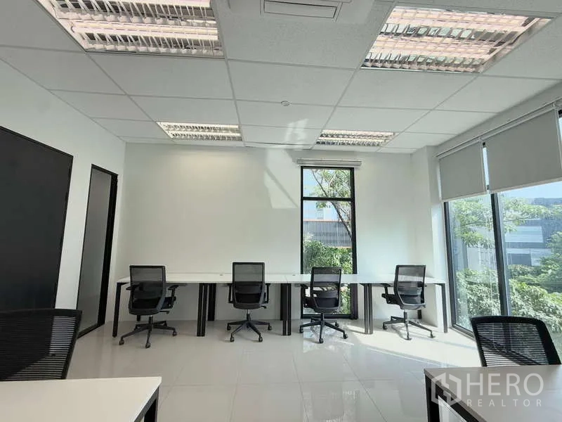 Office Space for rent in Huai Khwang, Bangkok - Light-filled workspace with a row of desks by floor-to-ceiling windows overlooking greenery.