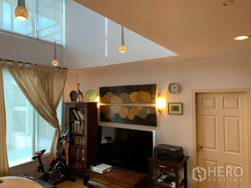 บ้าน ขายในSuan Luang, Bangkok - ห้องนั่งเล่นครอบด้วยสกายไลท์ มีผนังทีวี ชั้นหนังสือ และจักรยานออกกำลังกาย