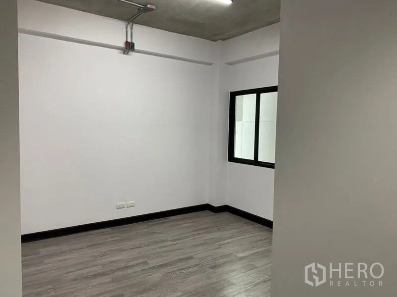 Office Space for rent - Private corner room with window, white walls, grey flooring, and exposed ceiling conduit in a modern office.