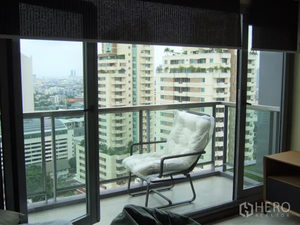 Condominium for rent or sale in Watthana, Bangkok - Private balcony with glass railing, lounge chair, and city view of high-rises.