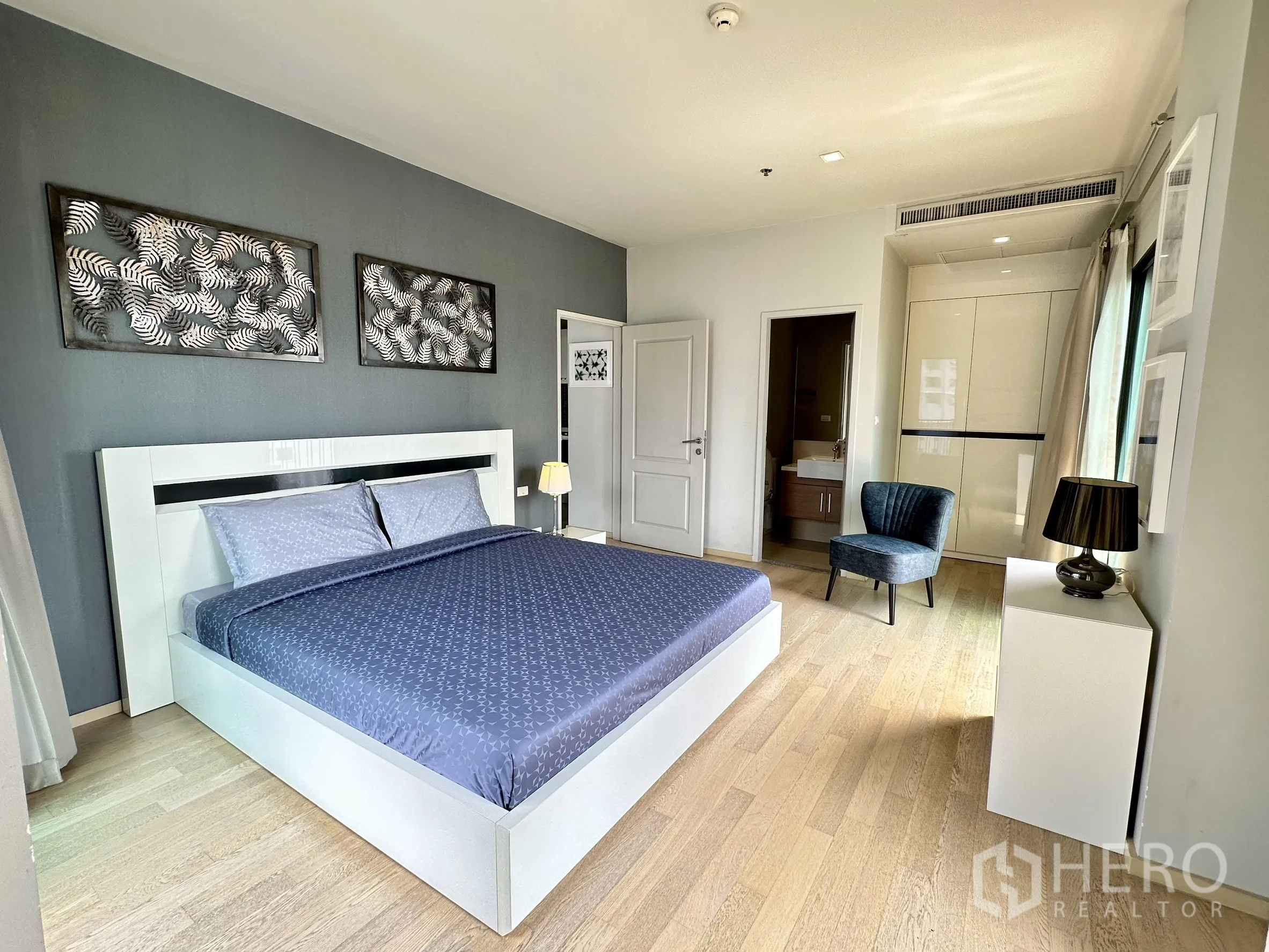 Condominium for rent in Bangkok - Bedroom showing king bed, built-in wardrobe, ensuite entrance and warm wood flooring.