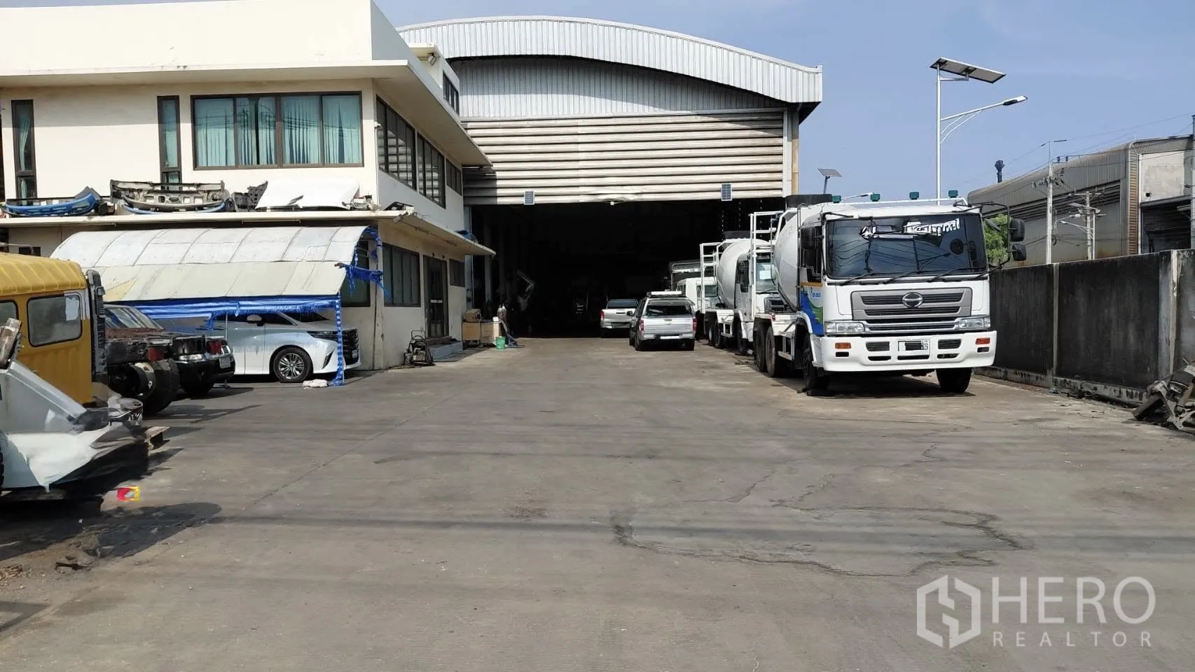 Warehouse for rent in Bang Phli, Samut Prakan - Paved truck yard with two-storey office building and large roller shutter entrance to the warehouse.