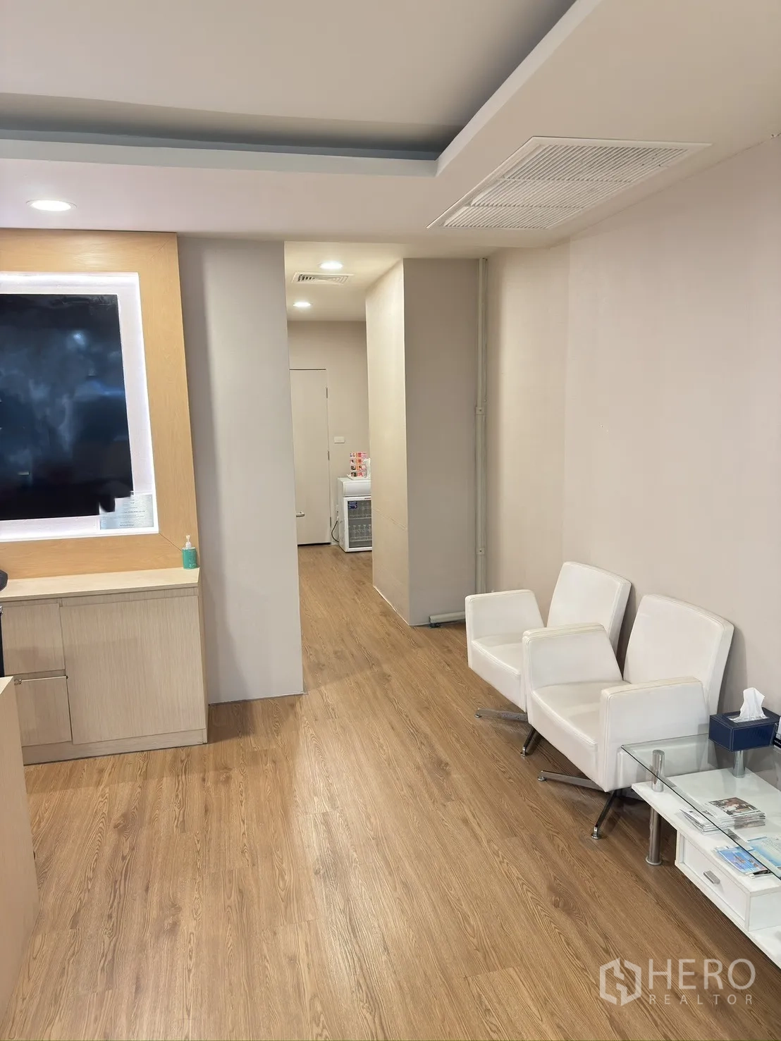 Retail Space for rent in Khlong Toei, Bangkok - Waiting area with white armchairs, a glass side table, and a corridor on wood floors.