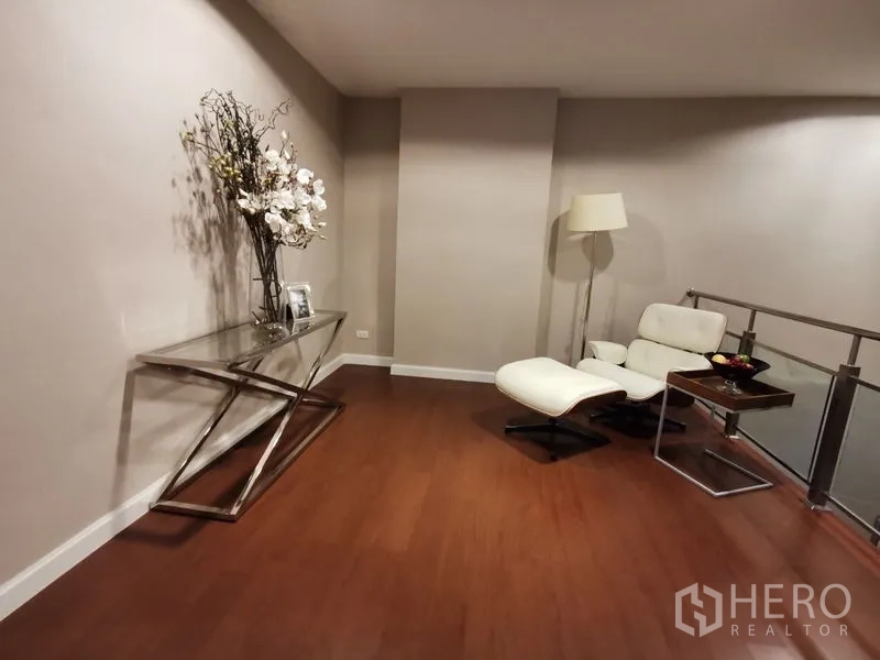 Condominium for rent or sale in Huai Khwang, Bangkok - Quiet reading nook with white recliner and ottoman, floor lamp, and sleek console table.