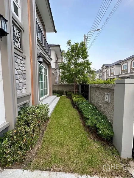 Detached House for rent - Side-yard lawn and shrubs beside the house facade with stone accents.