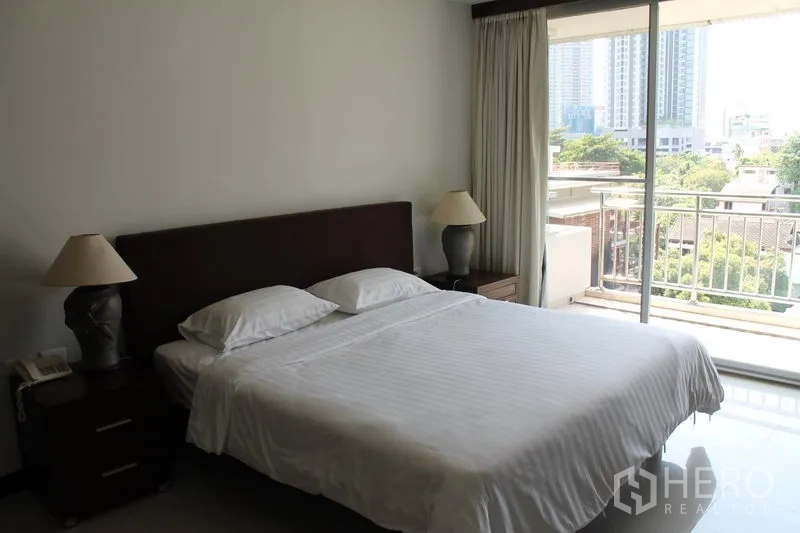 房间 出租在Bang Rak, Bangkok - 采光充足的卧室，推拉玻璃门通往阳台，眺望绿意与高楼。