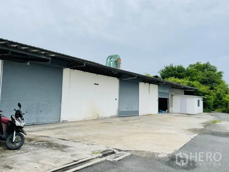 Factory for rent in Bang Pakong, Chachoengsao - Factory exterior with multiple roll-up doors, large forecourt and greenery along the site boundary.