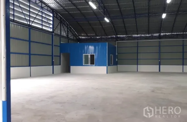 Warehouse for rent in Nong Chok, Bangkok - Warehouse interior featuring a built-in blue office room and wide open storage area beneath a high roof.