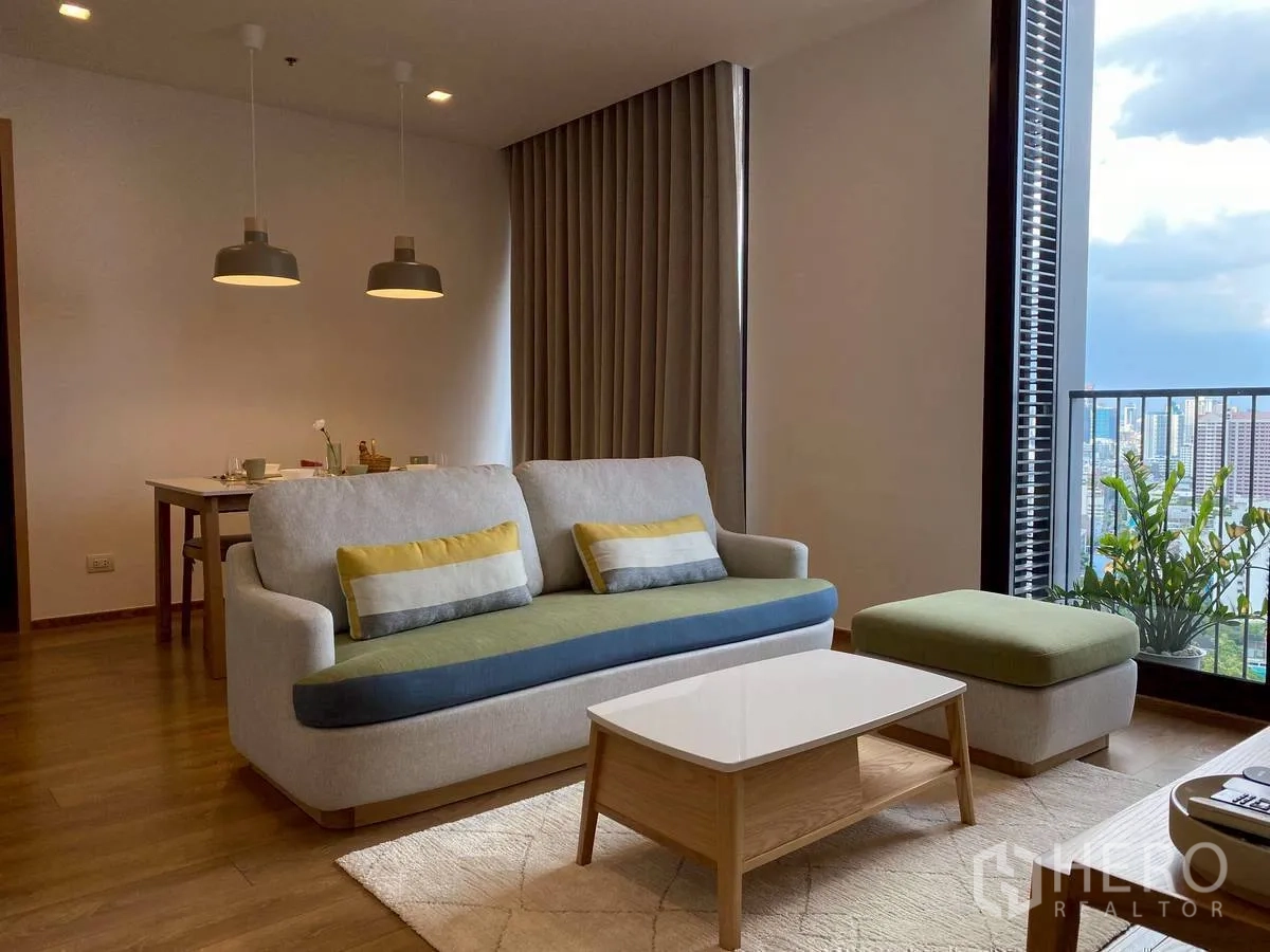 Condominium for rent in Watthana, Bangkok - Living area with sofa set, ottoman, coffee table, and balcony greenery.