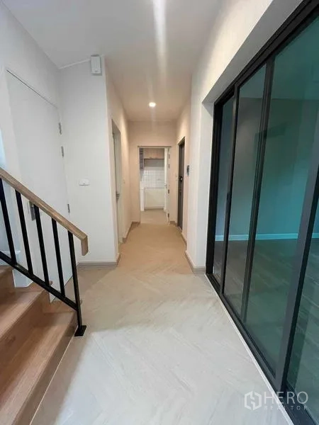 บ้าน ขายในBang Kruai, Nonthaburi - โถงชั้นล่างพร้อมผนังกระจก บันไดไม้ และทางเชื่อมไปครัวกับห้องน้ำ