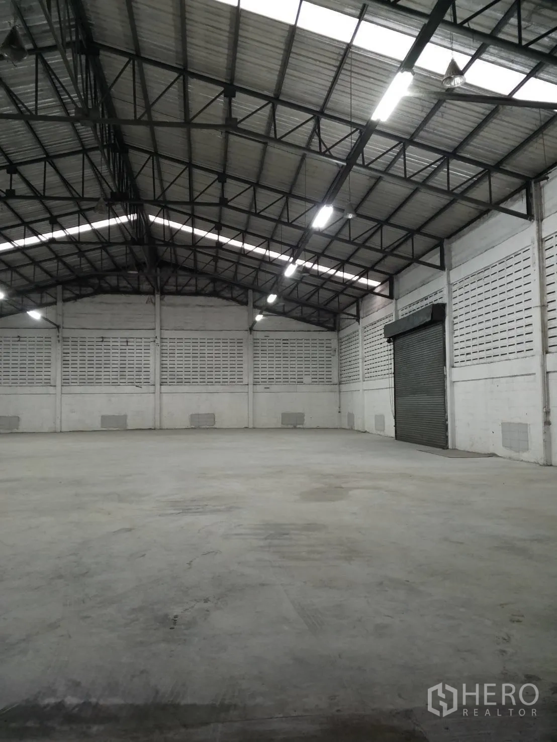 Warehouse for rent in Min Buri, Bangkok - Open-plan warehouse space showing high clearance, reinforced roof framing and a roller shutter entry.