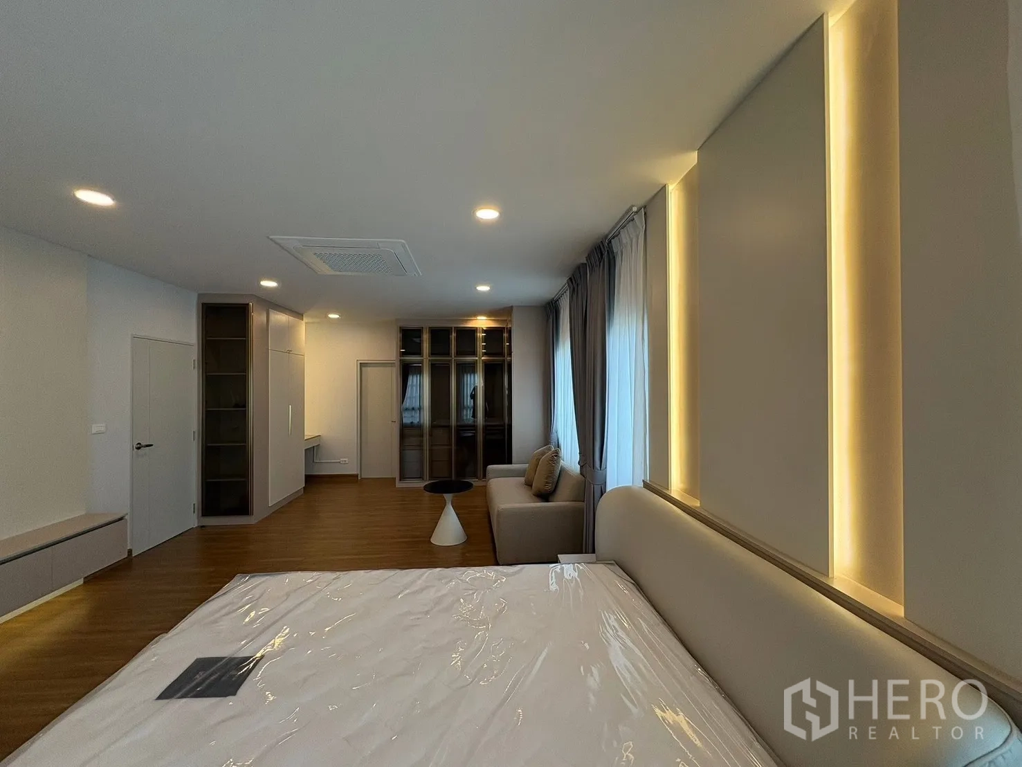 Detached House for rent in Bang Phli, Samut Prakan - Master bedroom with soft lighting, sofa corner, glass wardrobes and wood floor.