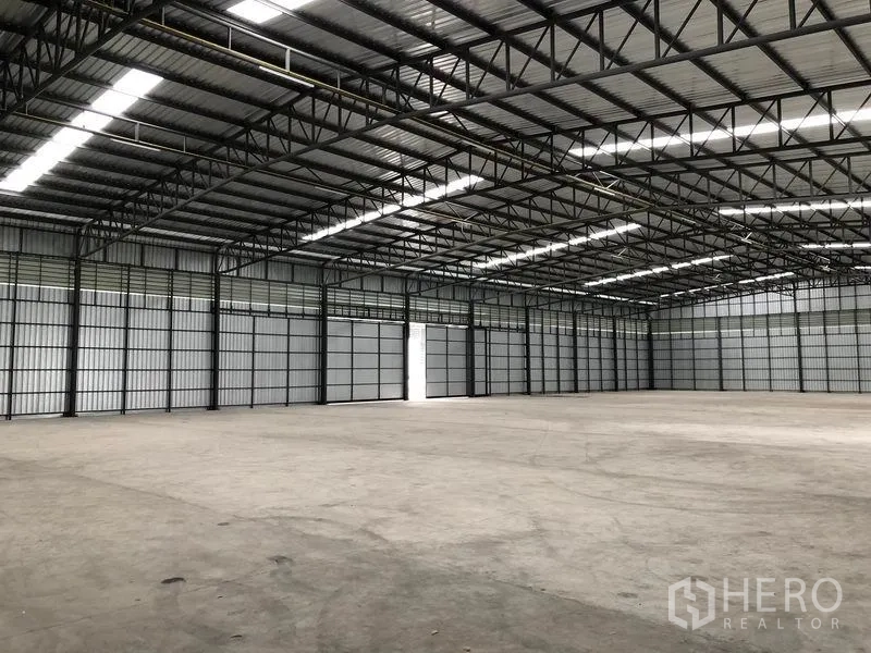 Warehouse for rent in Pathum Thani - Vast warehouse interior showing a high steel truss roof, skylight strips, and smooth concrete floor.