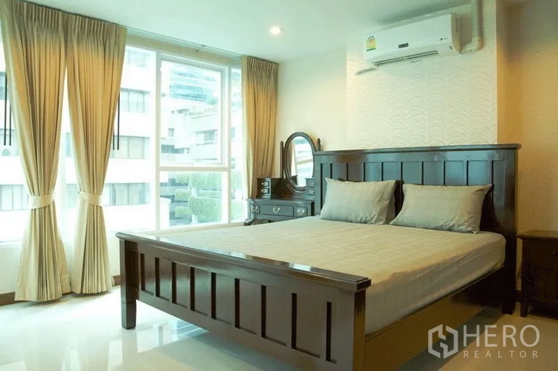 Condominium for sale in Watthana, Bangkok - Bedroom with dark wood bed, vanity, beige curtains and big windows for natural light.
