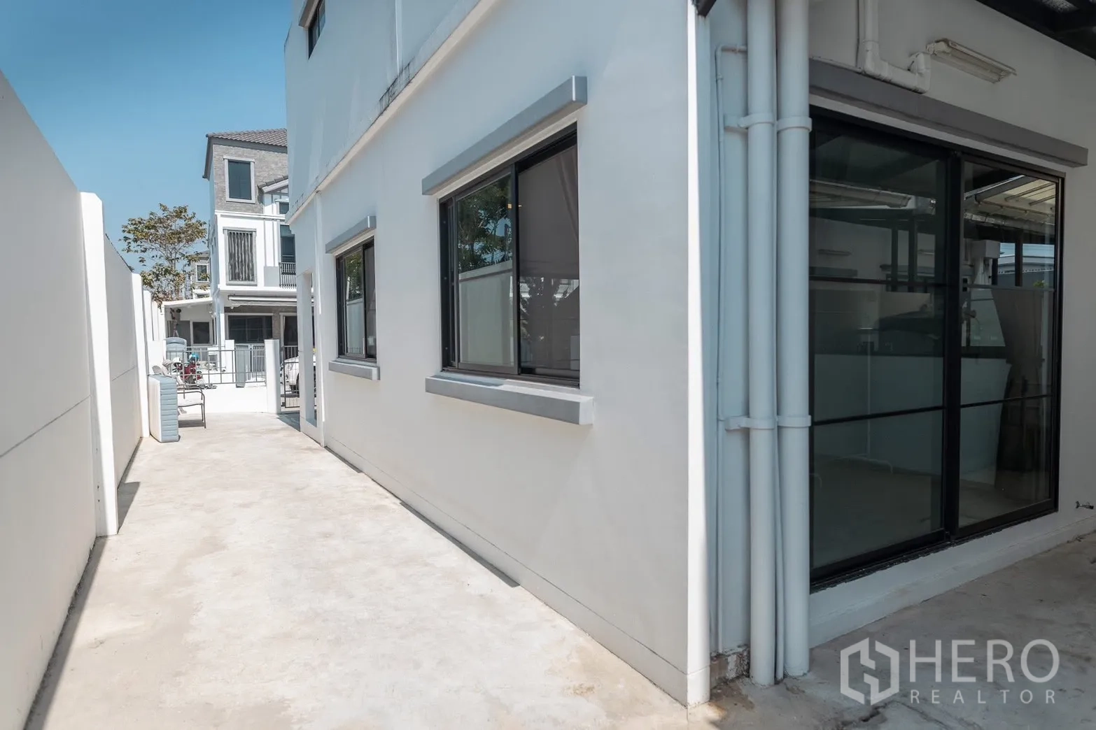 Townhouse for rent in Bang Phli, Samut Prakan - Side walkway of a modern white townhouse with sliding glass door and windows.