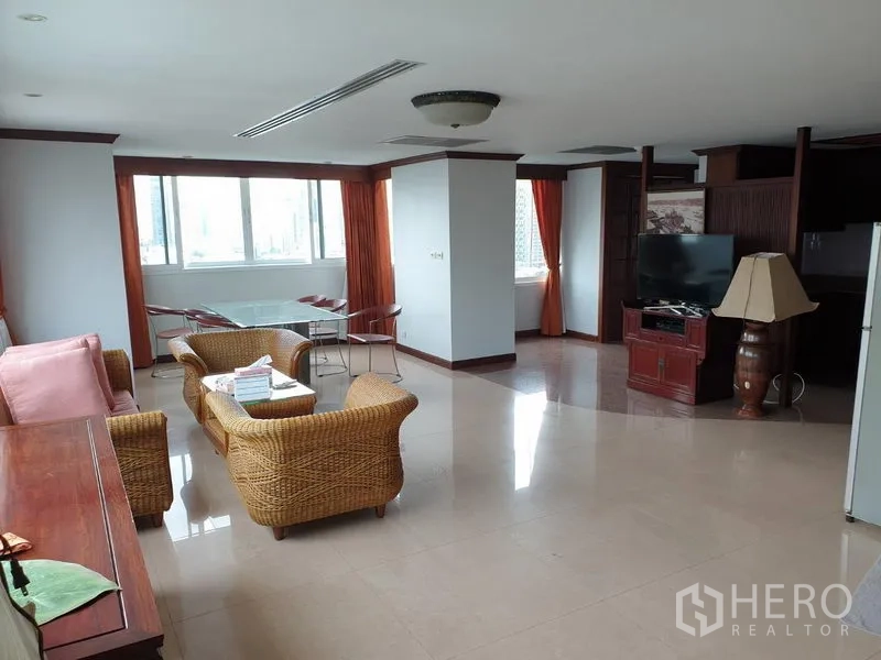 公寓 出租在Watthana, Bangkok - 开放式起居区，藤制座椅、瓷砖地面、电视柜与橙色窗帘的大窗。