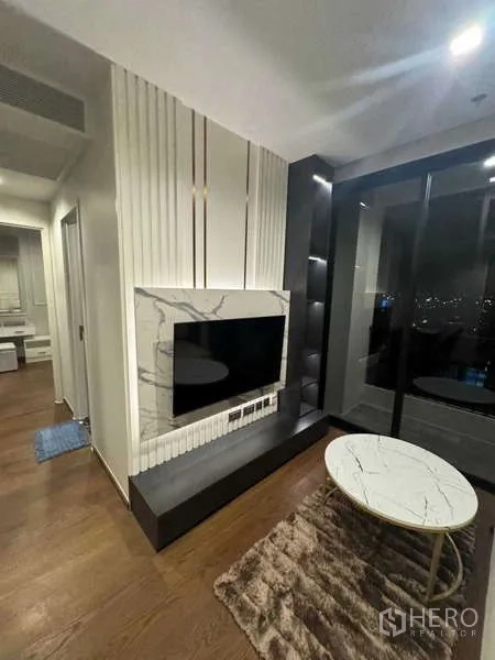 คอนโด ให้เช่าในKhlong Toei, Bangkok - ห้องนั่งเล่นมีผนังทีวีลายหินอ่อน กระจกเต็มบาน และประตูออกสู่ระเบียง