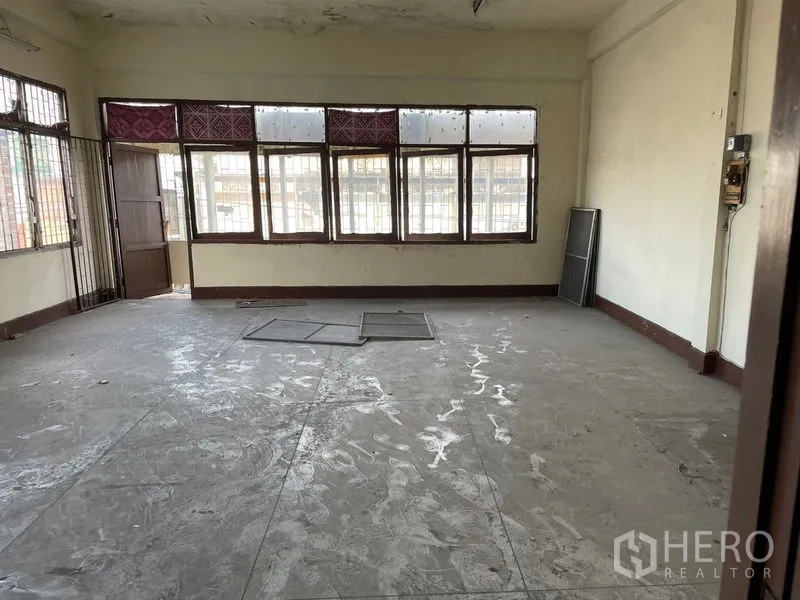 Shophouse for rent in Watthana, Bangkok - Front room with multiple street-facing windows and security grilles, suitable for display or seating.