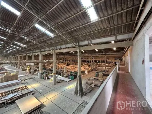 工厂 出租在Sai Noi, Nonthaburi - 俯视大型生产车间，高金属屋顶、采光带与多跨柱网，内有设备和物料。