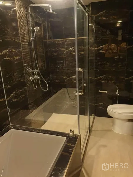 คอนโด ให้เช่าในKhlong Toei, Bangkok - ห้องน้ำสมัยใหม่พร้อมห้องอาบน้ำกระจก ผนังหินอ่อนสีเข้ม อ่างอาบน้ำ และโถสุขภัณฑ์