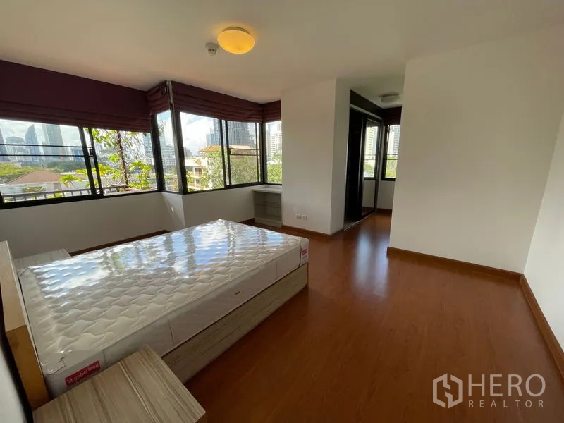 Condominium for rent in Watthana, Bangkok - Corner bedroom with wraparound windows offering greenery and city views.