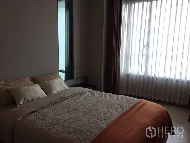 Condominium for rent in Ratchathewi, Bangkok - Master bedroom with large window and sheer curtains welcoming city light.