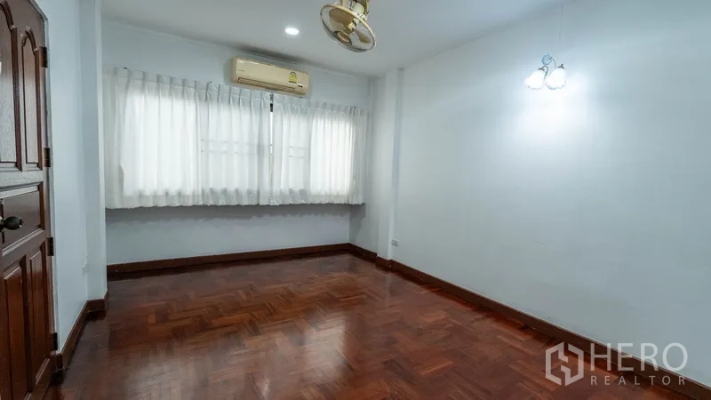 Townhouse for rent in Khlong Toei, Bangkok - Air‑conditioned bedroom with parquet floor and wide curtained window.