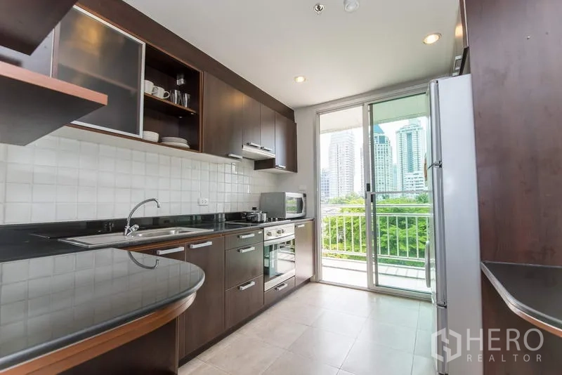 房间 出租在Sathon, Bangkok - 独立厨房，深色橱柜与嵌入式烤箱，落地门通向观景阳台。
