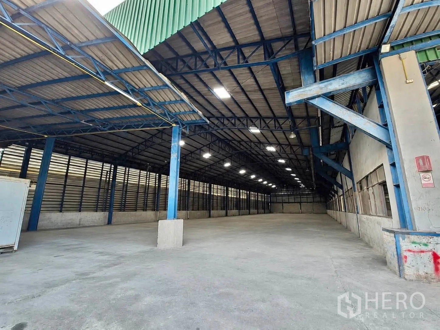 Warehouse for rent or sale - Long warehouse bay with high roof, ventilation panels, and clear open floor for storage.