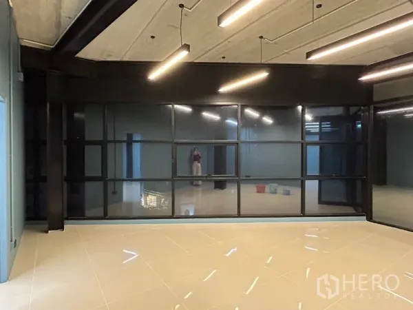 办公空间 出租在Chatuchak, Bangkok - 现代办公室，整面深色网格玻璃窗，线性吊灯与高反光地面。