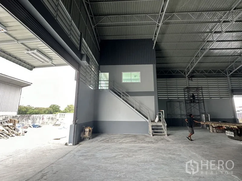 Factory for rent in Pathum Thani - Factory interior with high roof, mezzanine office block and staircase beside large roller door.
