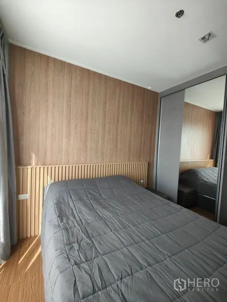 公寓 出租在Khlong Toei, Bangkok - 卧室配镜面衣柜，灰色被褥与木质墙板。