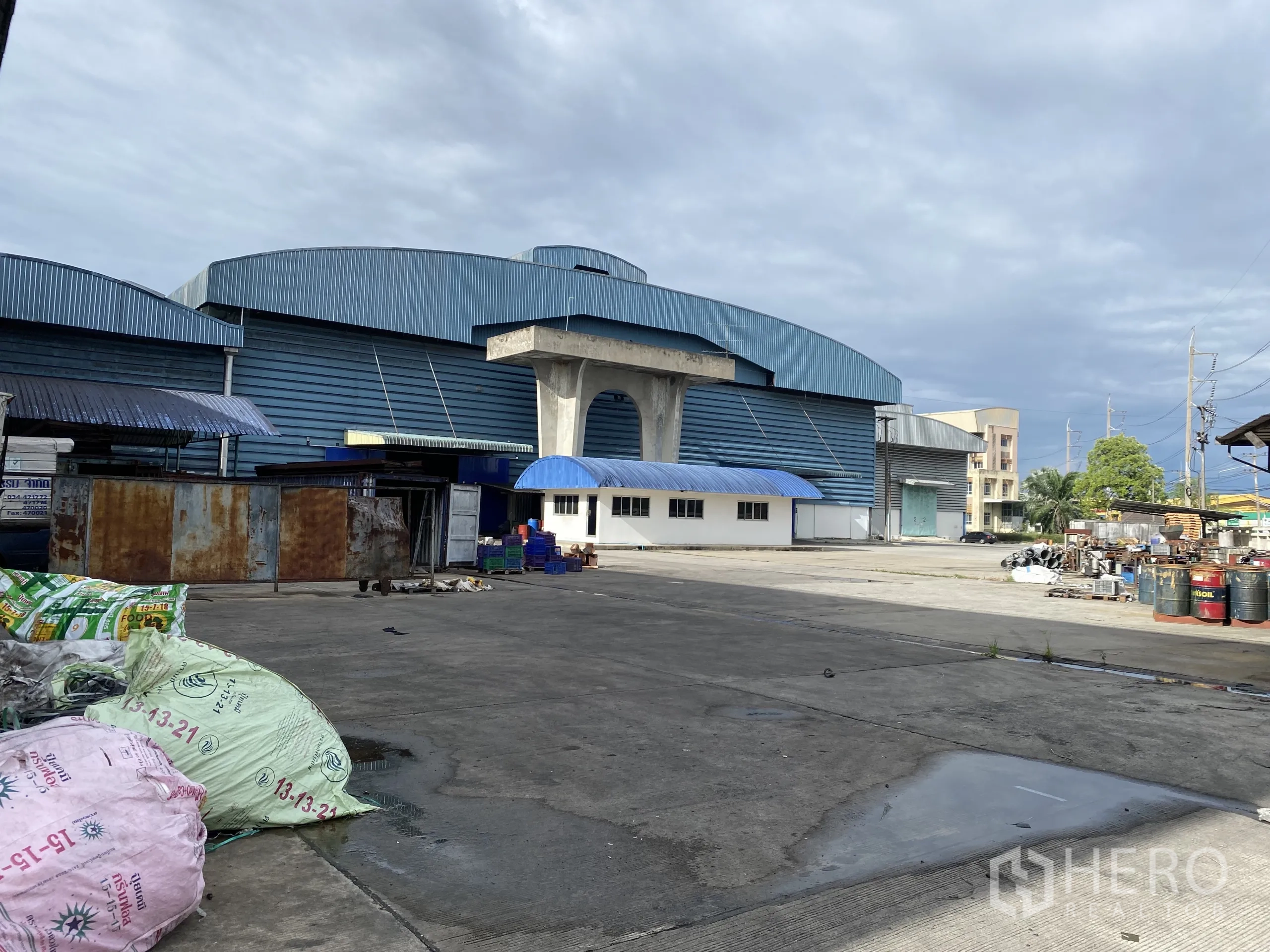 Factory for rent in Ban Phaeo, Samut Sakhon - Blue-clad factory buildings with expansive concrete yard and service areas for logistics.