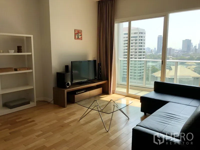 公寓 出租在Khlong Toei, Bangkok - 客厅配黑色皮沙发、玻璃茶几与电视柜，推拉落地门通向可观城市景观的阳台。