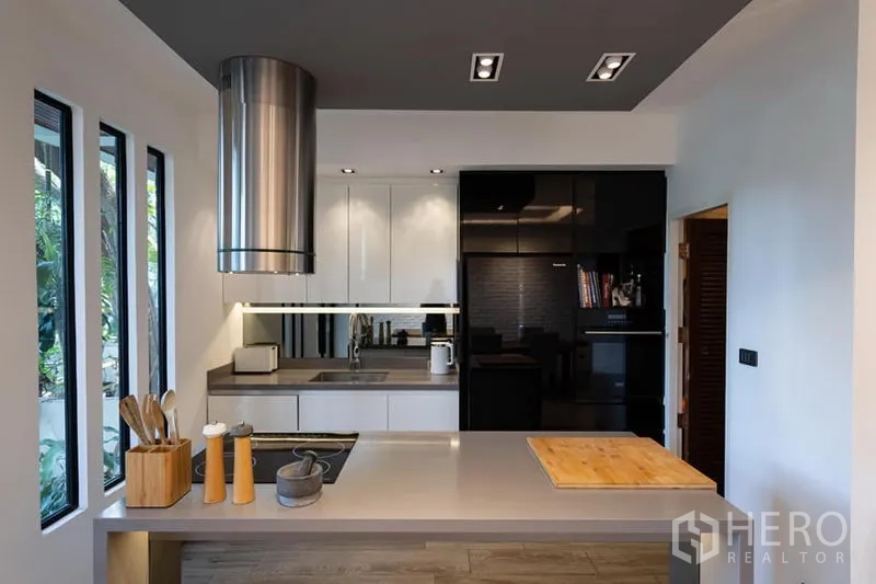 Townhouse for rent in Khlong Toei, Bangkok - Sleek kitchen with island cooktop, stainless hood and black-and-white cabinetry.