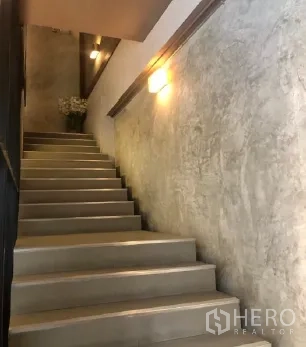 零售空间 出租在Pathum Wan, Bangkok - 室内楼梯配水泥质感墙面与壁灯，连接上下楼层。